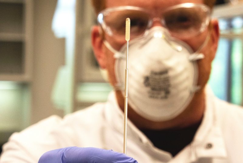 man holds a swab up to camera, up close focus on swab