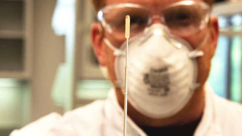 man holds a swab up to camera, up close focus on swab