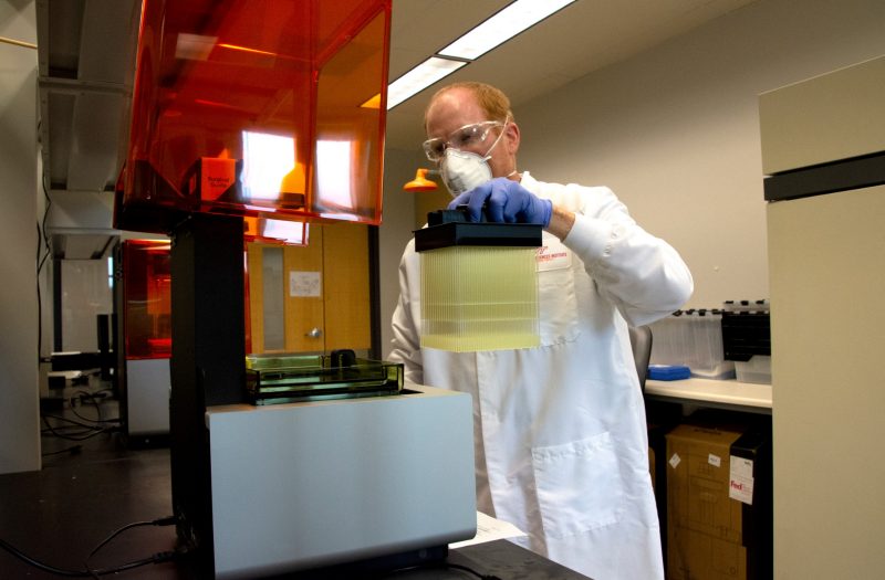 man pours liquid into 3D printer while wearing protective equipment