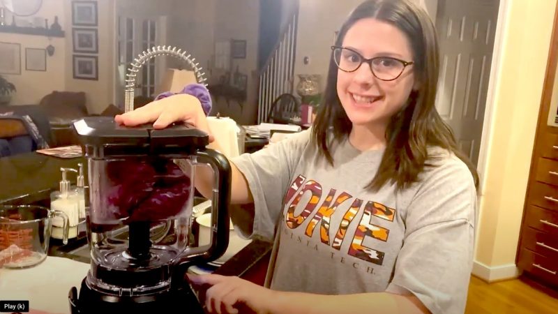 Woman stands in home kitchen with blender and smiles at camera