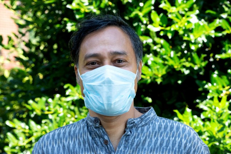 man wears masks and stands in front of green tree
