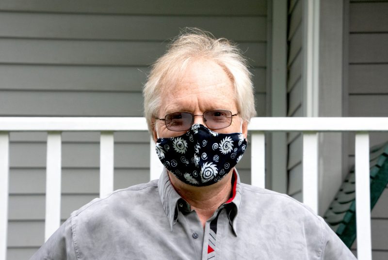 man stands in front of porch wearing a black mask