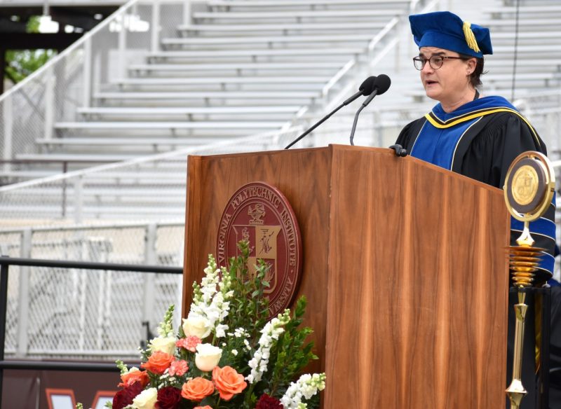 woman stands at podium in graduation regalia delivering speech