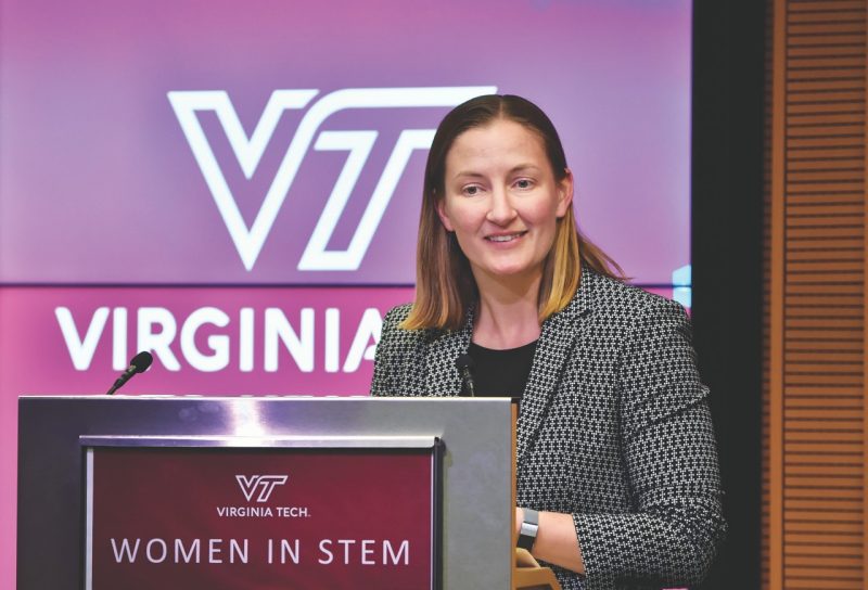 woman speaks at podium in tweed blazer with Virginia Tech logo in background