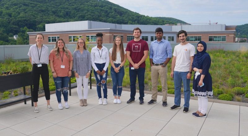 a group of student interns pose outside on a patio with mountains and medical building in background