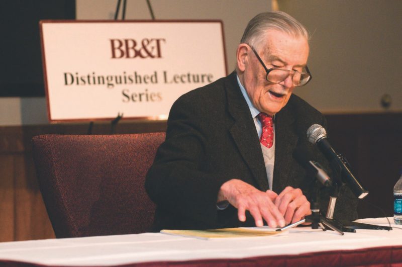 Buchanan sitting at table with microphone and talking off of notes.