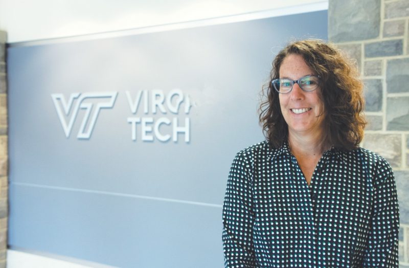 Trish stands by interior Hokie Stone wall and "Virginia Tech" sign.