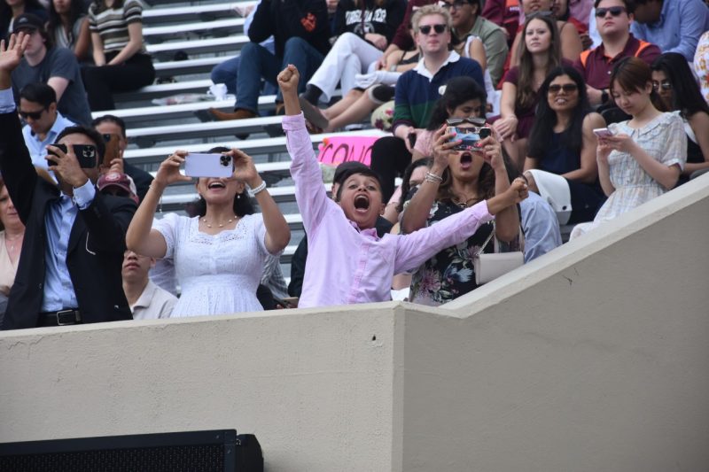 young boy enthusiastically cheers for graduates in the stadium