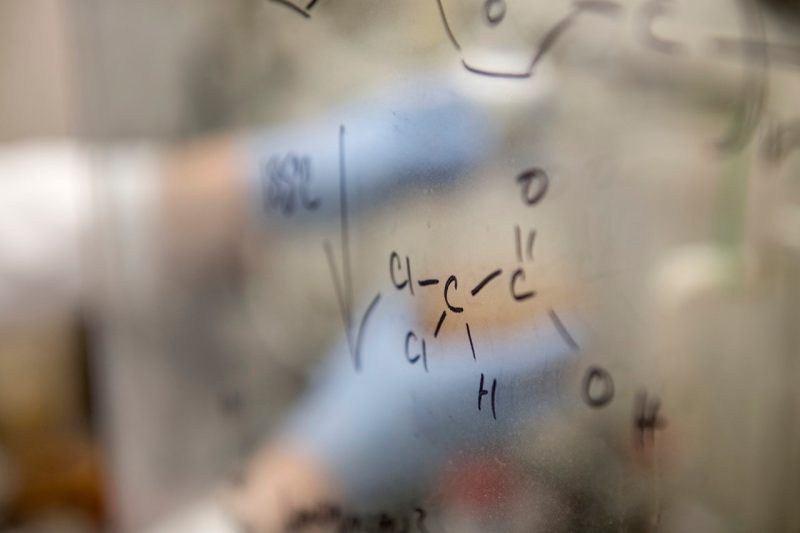 chemical structure in focus on window with blurred gloved hands in background